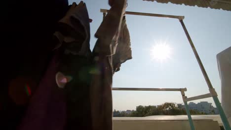 mientras el sol brilla en el balcón de un apartamento urbano de gran altura, una persona cuelga la ropa para que se seque
