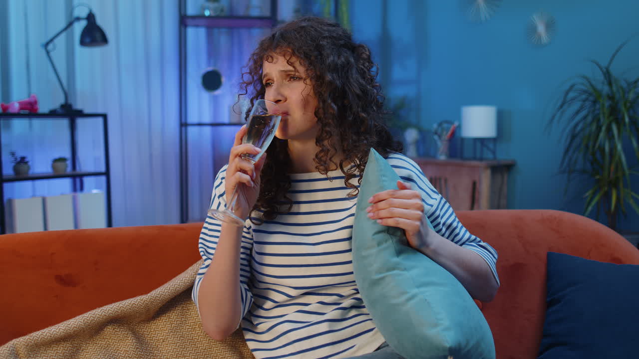 mujer sentada en un sofá mirando infeliz con un vaso de champán