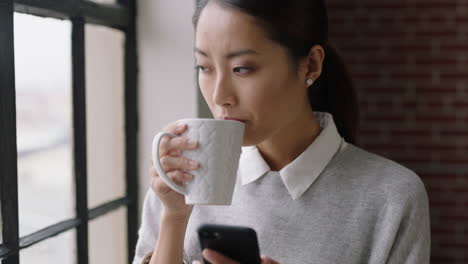 Hermosa-Mujer-De-Negocios-Asiática-Tomando-Café-En-Casa-Usando-Un-Teléfono-Inteligente-Disfrutando-De-Una-Mañana-Relajada-Navegando-Mensajes-Mirando-Por-La-Ventana-Planificando-Con-Anticipación-Mensajes-De-Texto-En-Redes-De-Teléfonos-Móviles