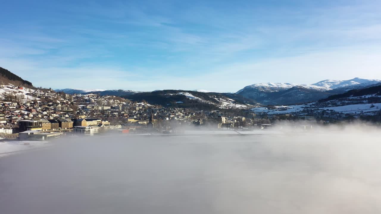 Acercándose a la ciudad de Voss, Noruega, a través de una neblina helada sobre el lago de agua dulce Vangsvatnet - Vista aérea al amanecer.