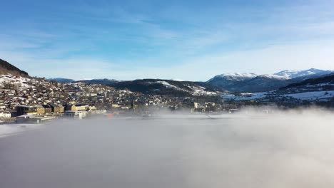 Approaching-city-of-Voss-Norway-through-frosty-haze-above-Vangsvatnet-freshwater-lake---Morning-sunrise-aerial