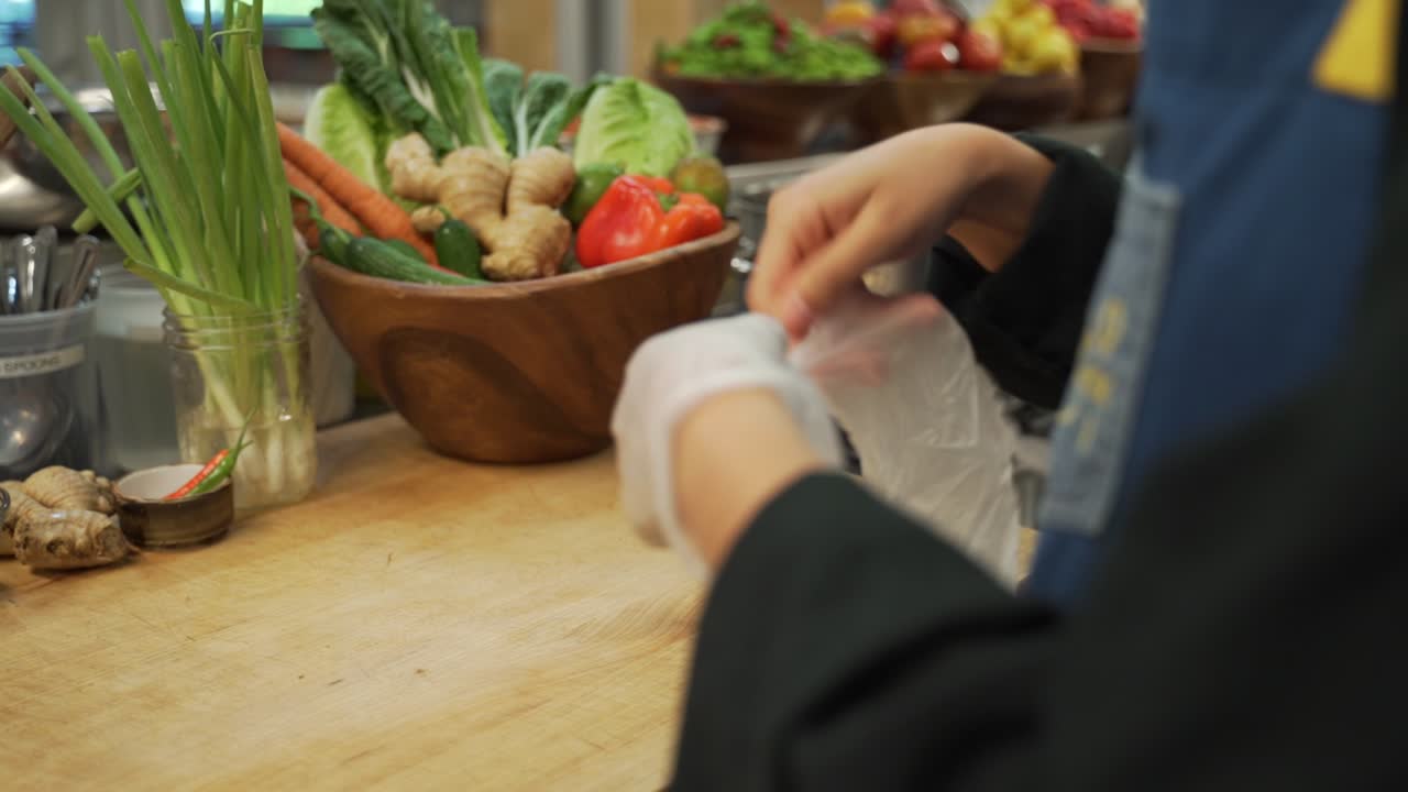This chef is showing safety and sanitation by putting on gloves before handling ingredients at a restaurant.