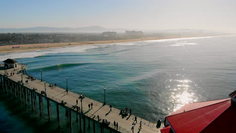 vuele sobre el muelle de la playa de huntington y la cena hacia el brillante amanecer en el océano pacífico con los hoteles hilton - hyatt a distancia del dron aéreo 4k