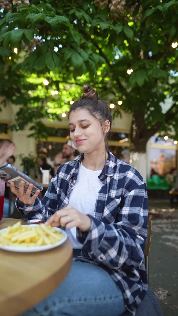 una mujer joven comiendo papas fritas en un café al aire libre