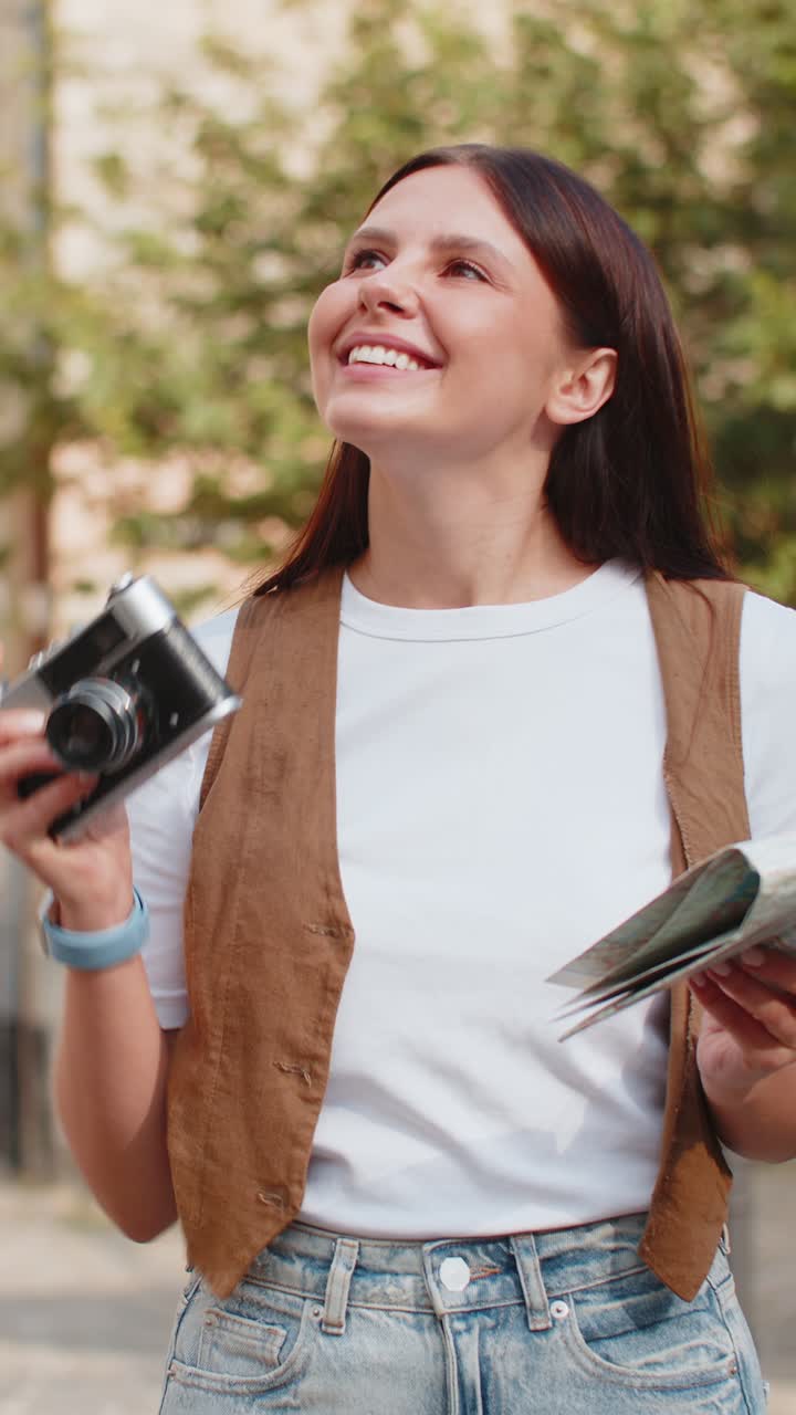 joven feliz viajera turista sosteniendo un mapa y tomando fotos usando una cámara retro en la calle de la ciudad
