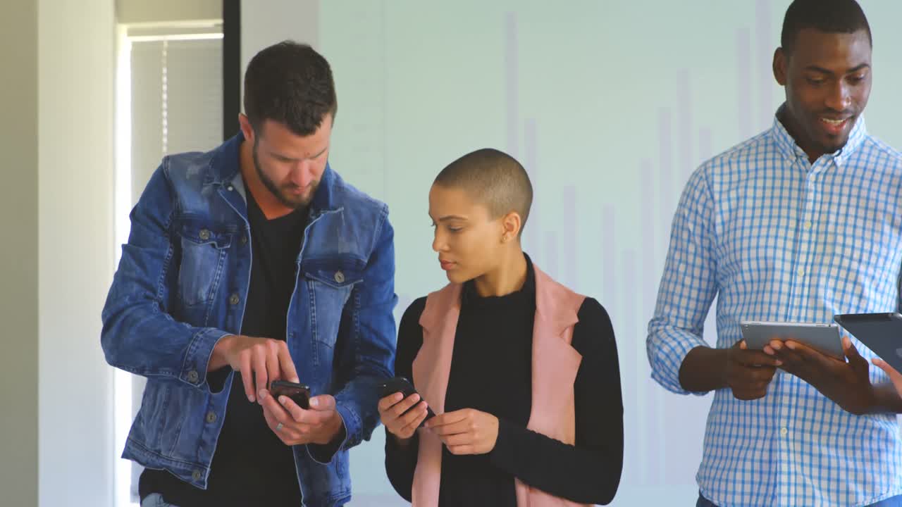vista frontal de un joven equipo de negocios de raza mixta trabajando en dispositivos multimedia en una oficina moderna 4k