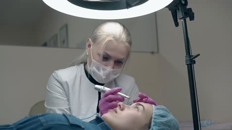 una mujer se sienta cerca del paciente y aplica maquillaje permanente