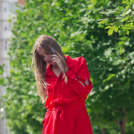 beautiful girl outdoors. pretty young woman with long straight hair standing near the green tree and talking on the phone in the city. slow motion.