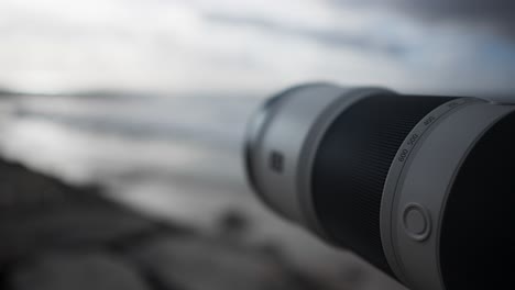 Close-up-of-a-telephoto-lens-pointing-at-the-ocean