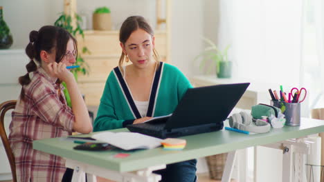 mother helps her daughter learn by solving homework on a laptop