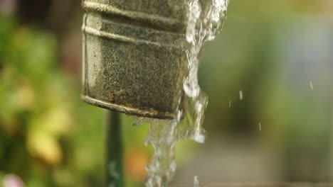 water falls in slowmotion in a garden from a diy outdoor faucet overflowing a rustic bucket