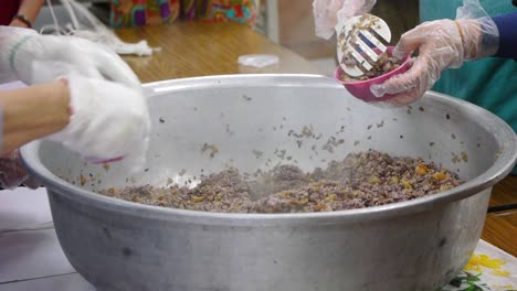 la mezcla de arroz morado y carne de cerdo se pasa de un tazón grande a pequeños tazones rosados para medir el peso en una zona de cocina concurrida