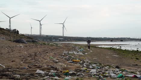 persona caminando por una playa contaminada con un parque eólico visto al fondo en son hai, vietnam