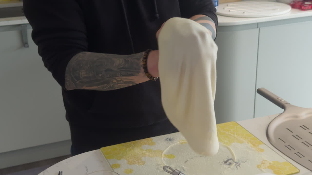 Pizza enthusiast demonstrates skilful dough tossing and preparation in a kitchen, enhancing the pizza-making experience at home.