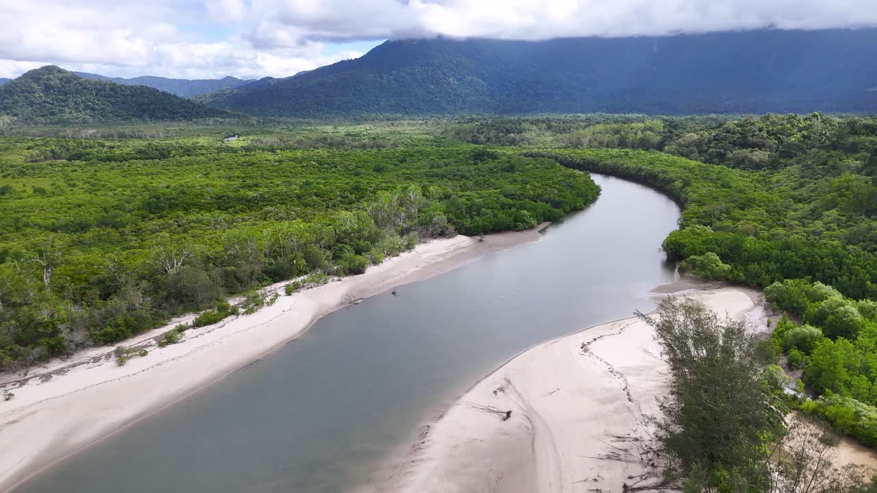 Drone glides above winding river, lush rainforest, and sandy beach under bright, natural daylight