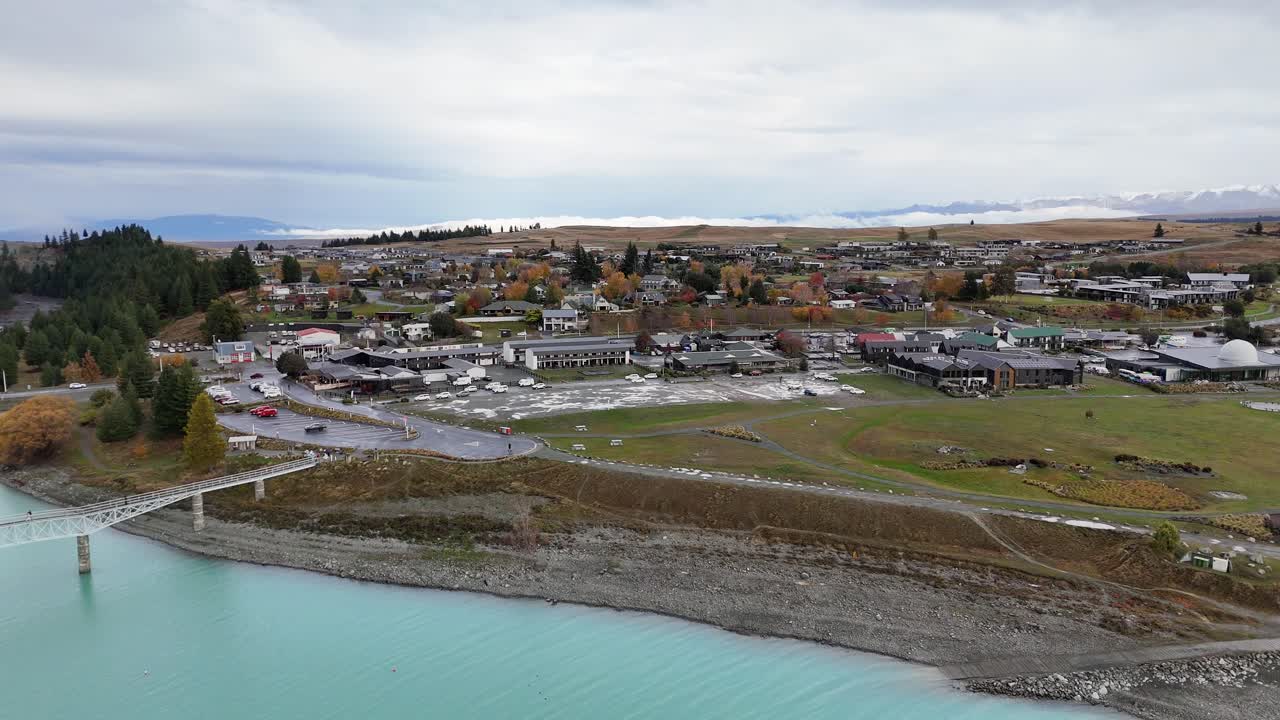 Aerial footage captures Lake Tekapo's turquoise waters and surrounding town under overcast skies, showcasing serene landscapes and autumn foliage