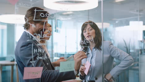 Geschäftsleute,-Die-Haftnotizen-Verwenden.-Junger-Teamleiter-Beim-Brainstorming-Mit-Kollegen,-Die-Ideen-Auf-Ein-Glas-Whiteboard-Schreiben,-An-Einer-Lösung-Arbeiten-Und-Strategie-Teamarbeit-In-Einer-Bürobesprechung-In-4K-Diskutieren