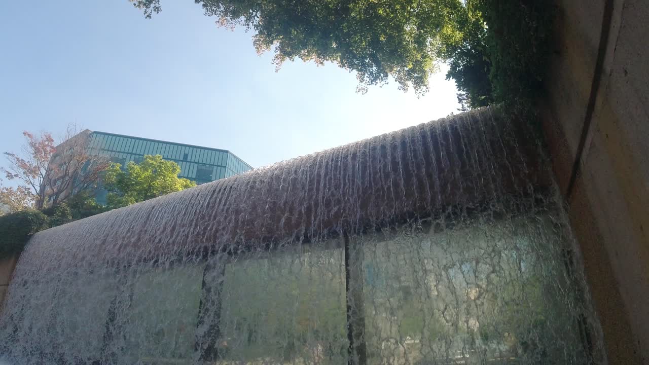 perspectiva de cascadas modernas de hormigón que bajan de un juzgado futurista con vidrio espejado bajo cataratas que muestran un reflejo de la gente que camina con un horizonte claro de edificios de oficinas de vidrio 4-4