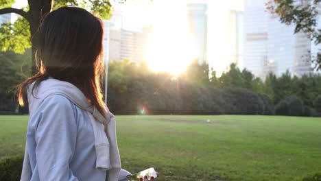 4k: beautiful asian woman listening music under sun flare at park,shanghai,china