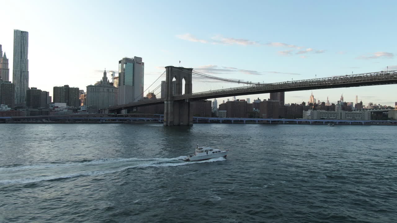 브루클린 다리와 뉴욕 맨해튼 시내가 있는 동쪽 강에서 맑은 여름 저녁 해질녘 배경에 있는 보트의 광각 공중 추적 샷