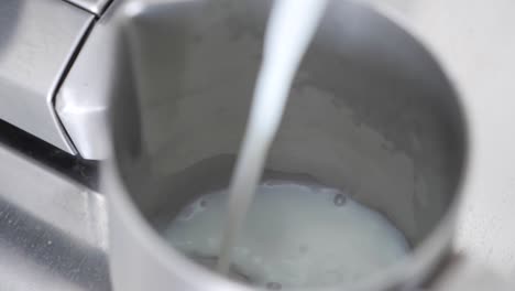 slow motion close up top down angle of milk pouring into a milk pitcher to make a latte