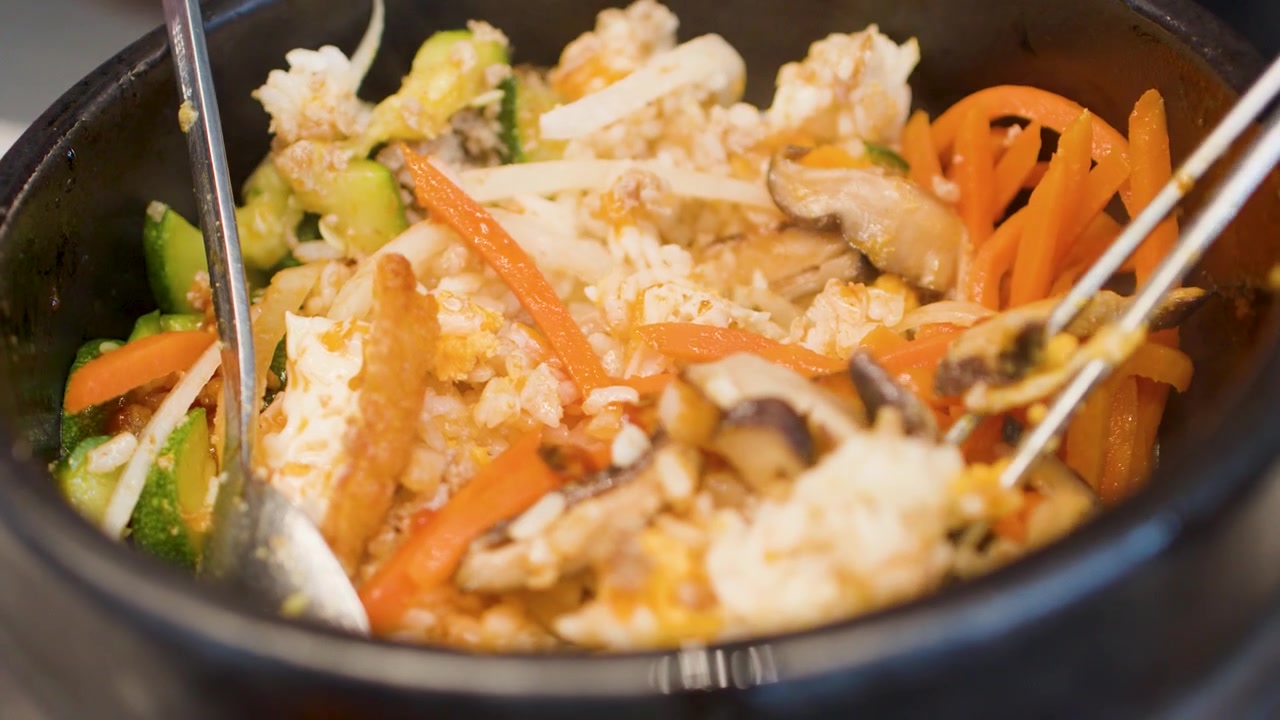 Bidikan close-up pencampuran bibimbap dengan sayuran dan nasi dalam mangkuk batu panas