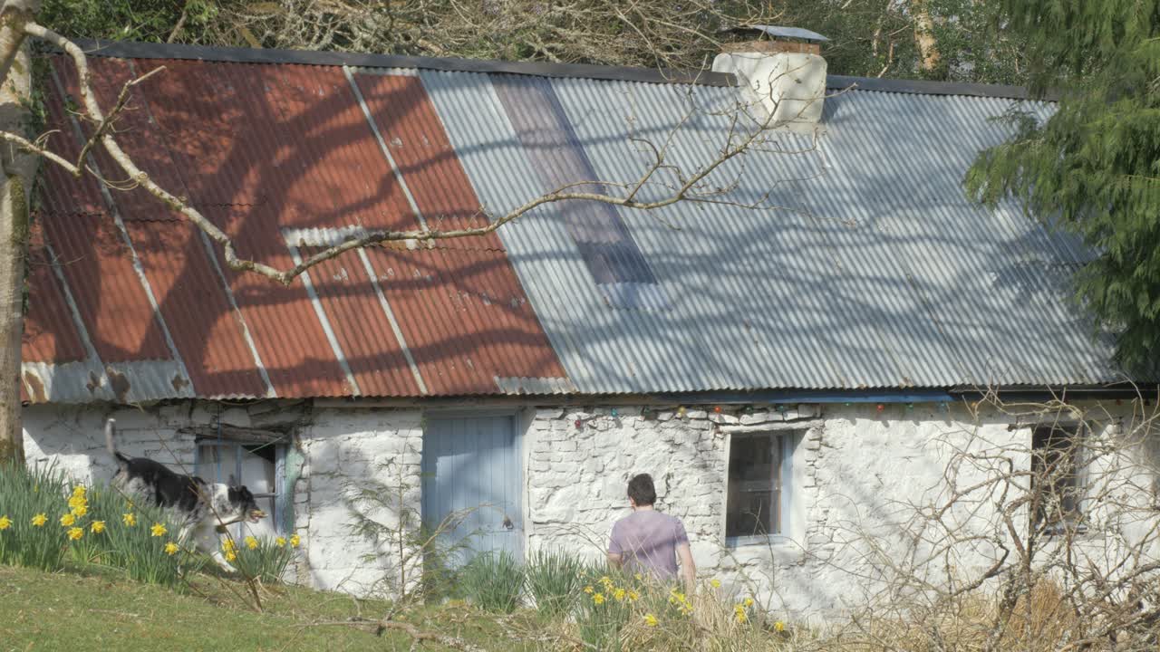 Young man enters repaired Irish cottage with corrugated roof