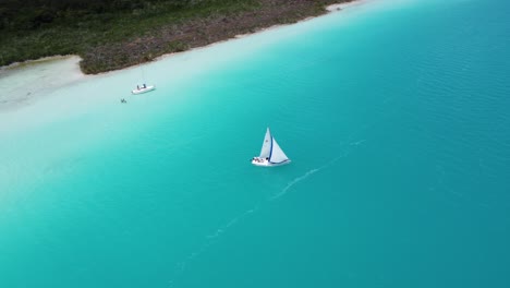 a sailboat on the vibrant blue waters of bacalar lagoon, with serene surroundings, aerial view