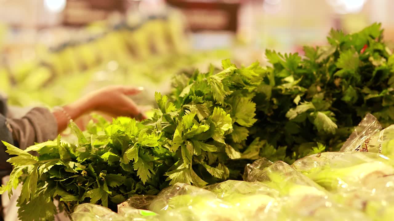 A person examines and picks celery in a well-lit supermarket produce section