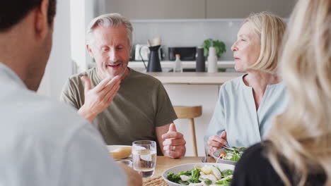 Familia-Con-Padres-Mayores-E-Hijos-Adultos-Comiendo-Juntos-Alrededor-De-La-Mesa-En-Casa