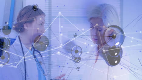 Two female doctors with stethoscopes reviewing tablet data in clinic, with digital network overlay
