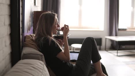 healthy young woman sitting on a couch holding a bowl of porridge looking relaxed and comfortable