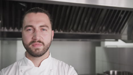 portrait of happy caucasian male chef with beard smiling in kitchen, copy space, slow motion