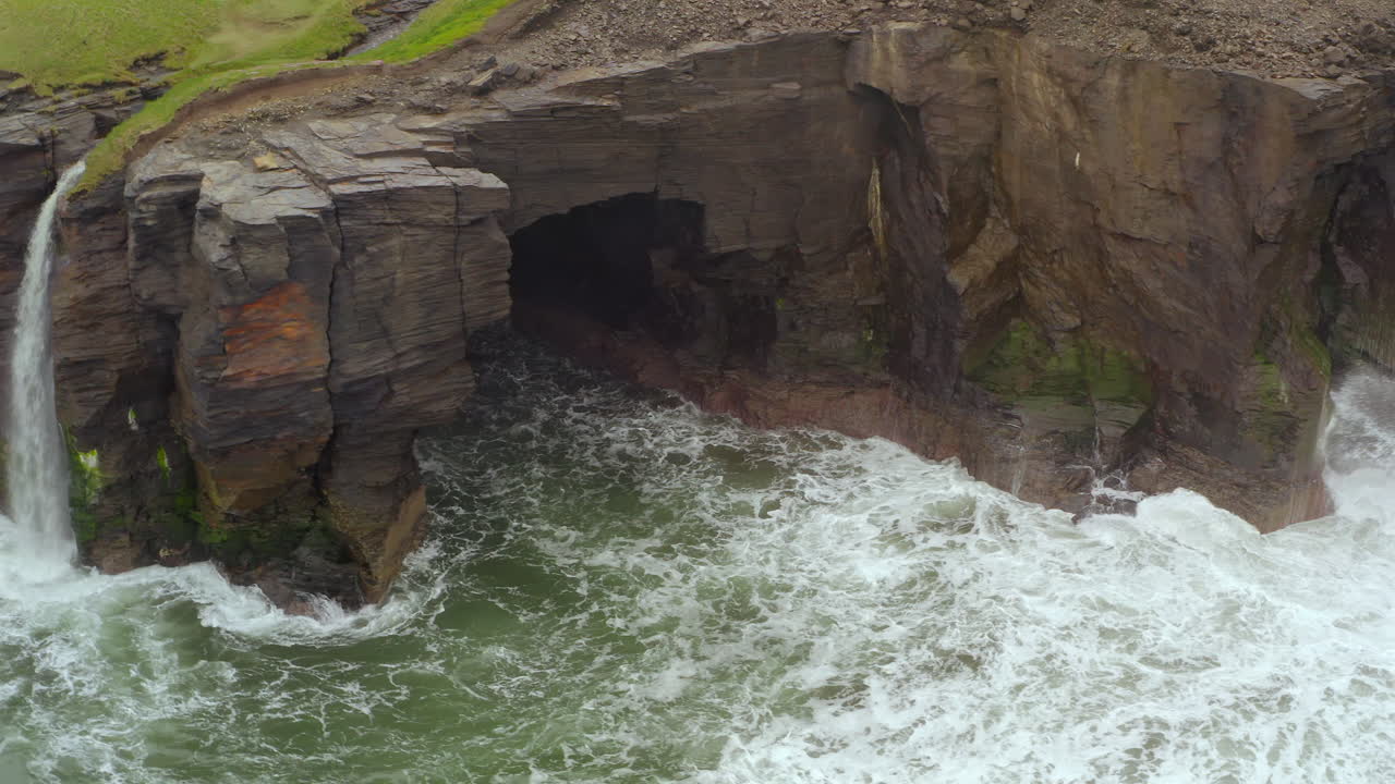 Dynamic aerial reveals sea caves and waterfall at Cliffs of Moher. Doolin,