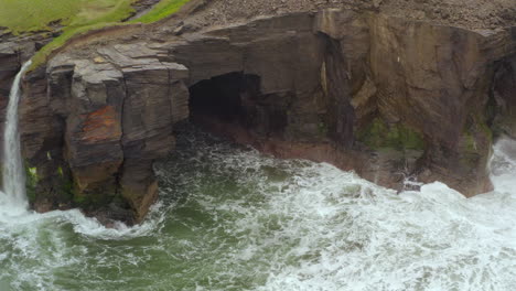dynamic aerial reveals sea caves and waterfall at cliffs of moher. doolin,