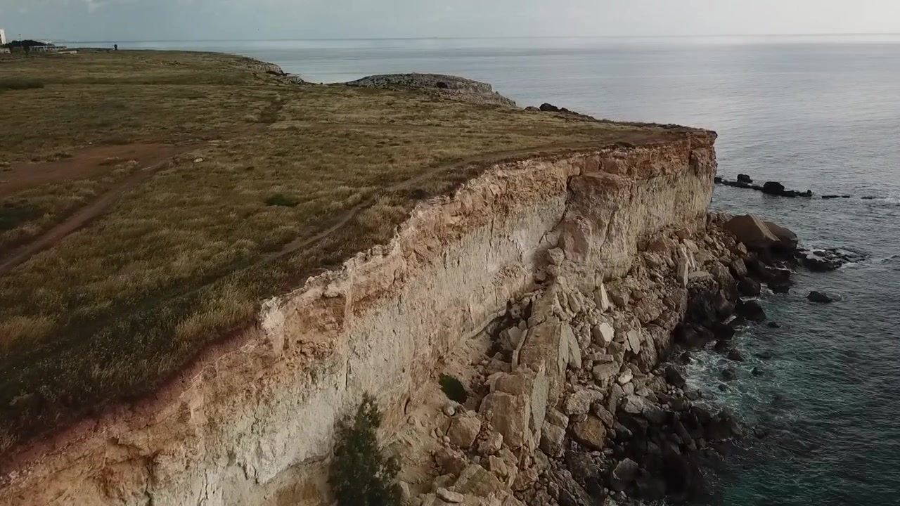 Drone flies forward along rugged limestone cliffs and rocky shoreline on the Mediterranean coast of Siracusa, Sicily, Italy.