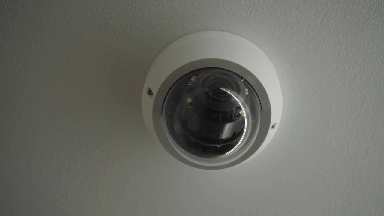 White dome-style security camera mounted on the ceiling of an indoor space.