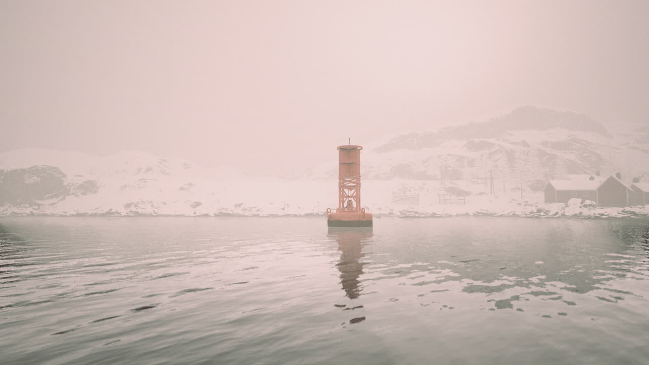 Foggy winter landscape with buoy and snow covered rocks by the water