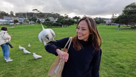 una mujer alimentando a una cacatúa en un parque de hierba