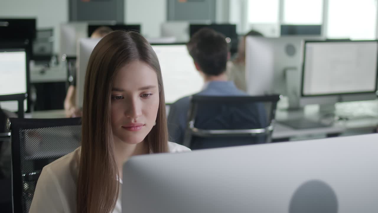 Attractive Young Woman Working on Decktop Computer While Working in Big Open Space Office. Portrait of Positive Business Female Looking at Computer Screen Indoors