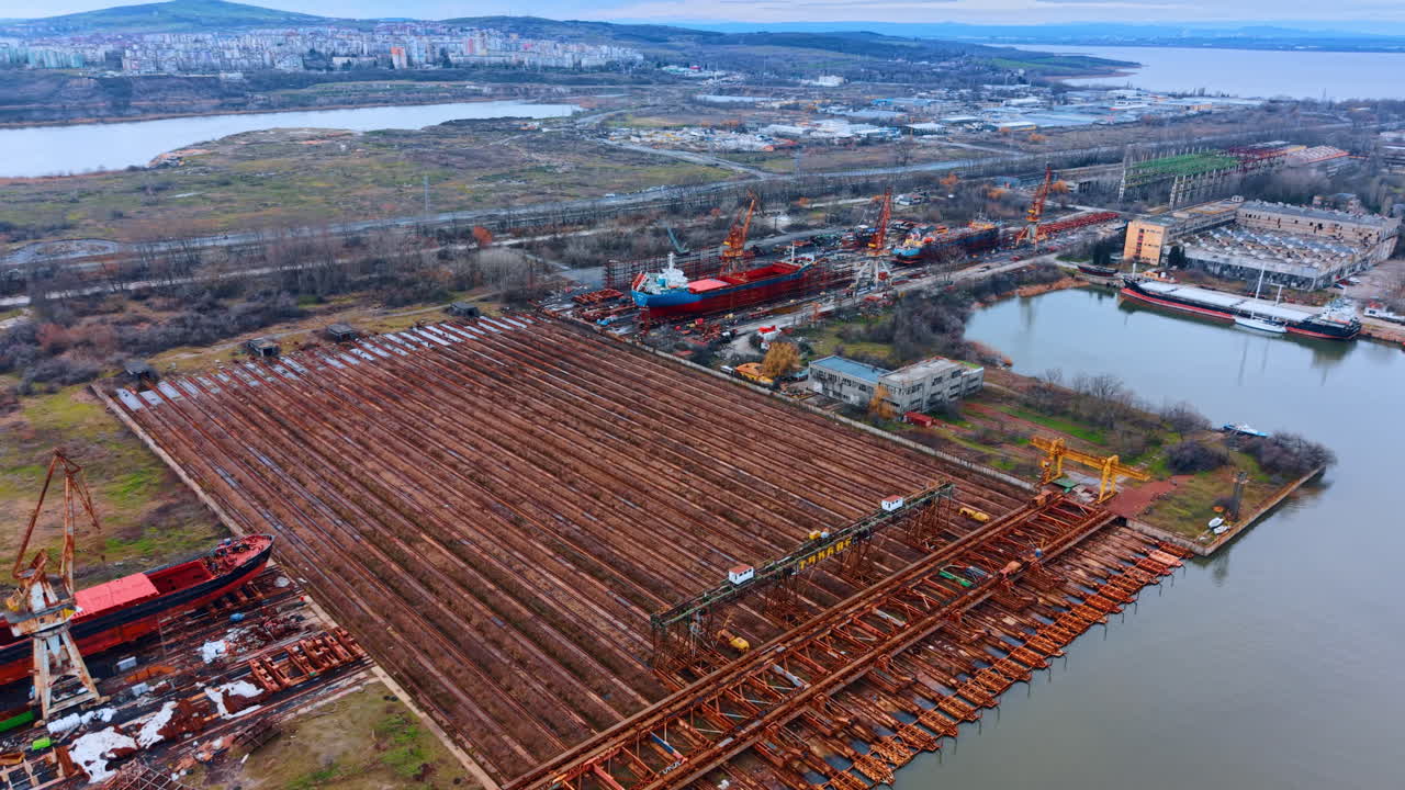 Vista panoramica dei moli del cantiere navale e della costruzione di navi. Veduta aerea di zona portuale industriale con scali di alaggio, gru e navi incompiute sullo sfondo di uno skyline cittadino
