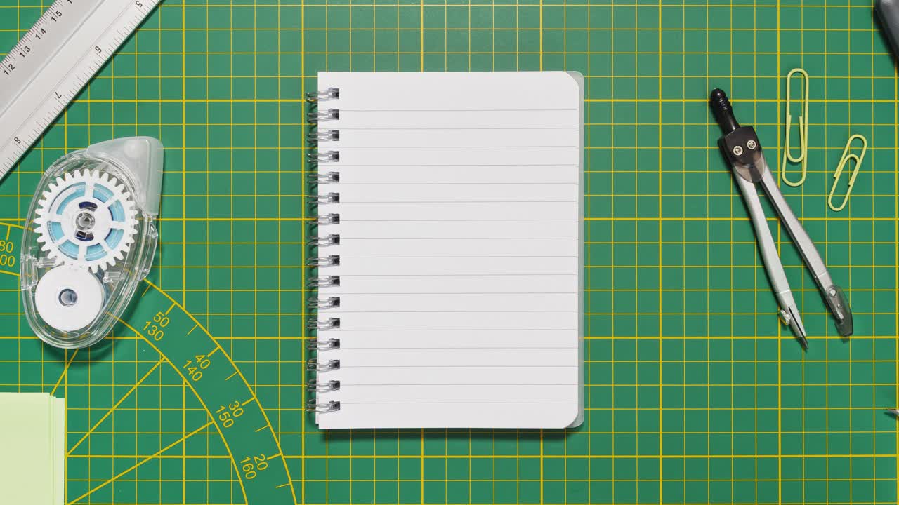Stop motion stationery frames a lined spiral notebook on green cutting mat, providing loopable copy space