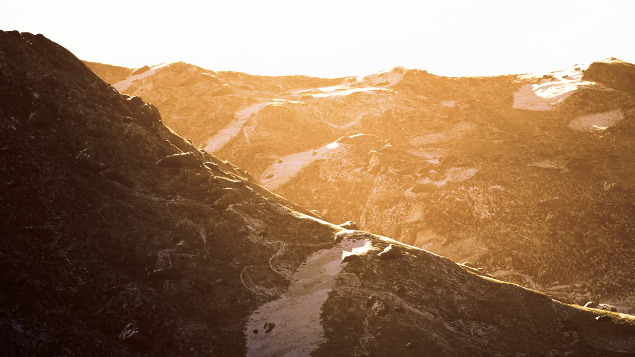Golden hour sunlight illuminates rugged mountain landscape at dusk