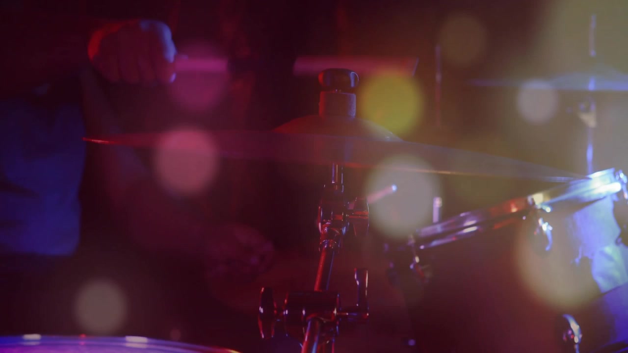 Bacchetta che entra, batterista che alterna colpi su rullante e piatto per il ritmo in studio musicale, bokeh sulla batteria.