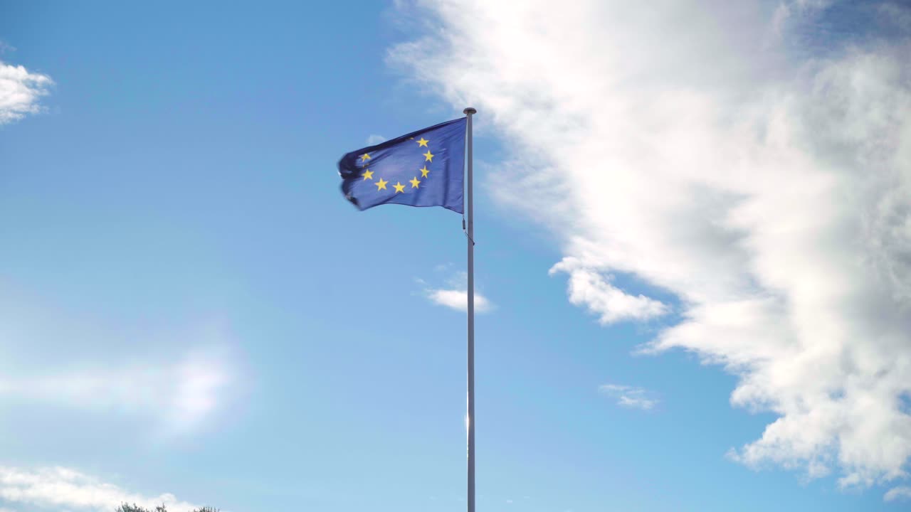 Bandiera europea che sventola da sola con forte vento su un cielo blu e nuvoloso, simbolo dell'alleanza dell'Unione Europea.