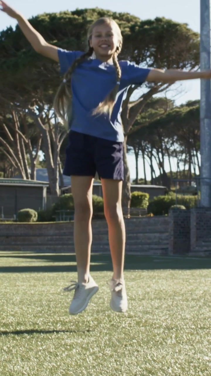 Video verticale: Un bambino con le trecce che fa salti in alto giocando sull'erba sintetica, con maglietta blu e pantaloncini blu scuro.