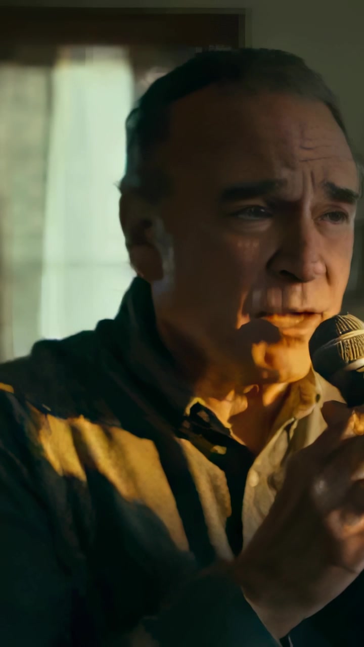 Vertical video: Singing senior man opening line at home, holding mic, wearing shirt, emoting