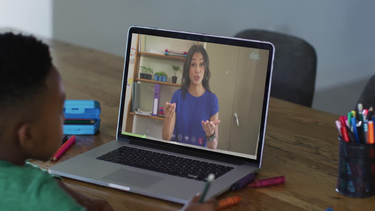 niño afroamericano sentado en un escritorio usando una computadora portátil teniendo una lección escolar en línea
