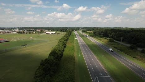 Eine-Luftaufnahme-Einer-Langen-Straße-Neben-Einem-Grünen-Feld-Mit-Einer-Baumreihe,-Die-Sie-Trennt