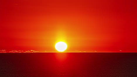 el lapso de tiempo del sol caliente que se eleva a través del cielo rojo claro sobre el cuerpo de agua